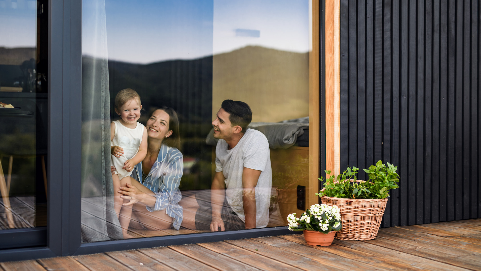 Een man en een vrouw met hun dochter zitten achter een alumiunium raam met een grote glimlach